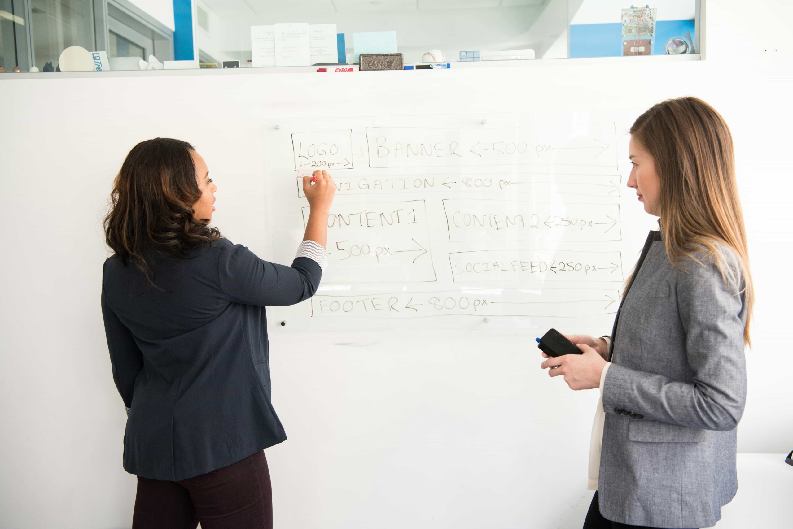 two women in front of a whiteboard